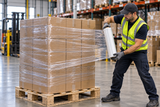 Clear hand stretch wrap being applied to stacked cartons on a pallet